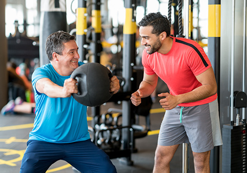 A man is doing a weighted squat and talking to his personal trainer